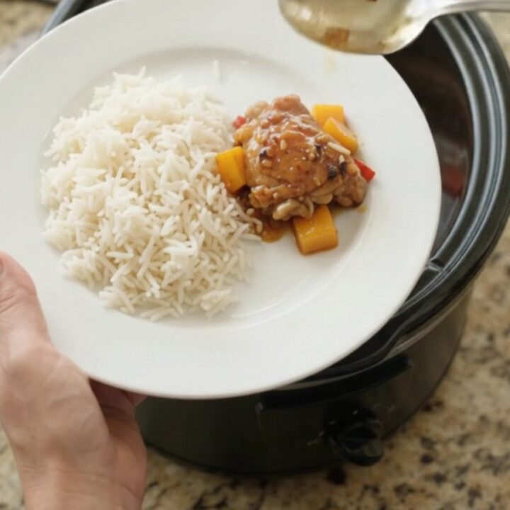Slow-cooker mango honey soy chicken thighs in a black crockpot, topped with mango cubes and red peppers