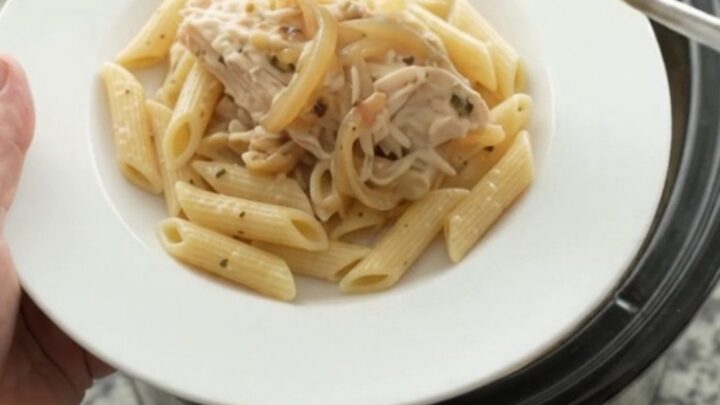 Slow cooker filled with shredded turkey, onions, and melted mozzarella in a creamy sauce