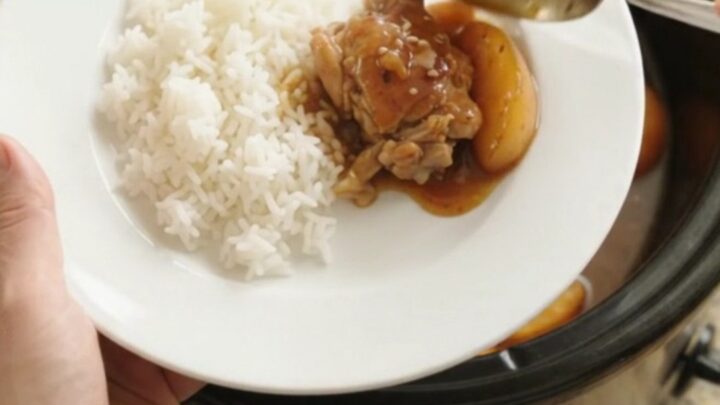 Slow cooker with caramelized peach teriyaki chicken thighs, glistening sauce, sesame seeds