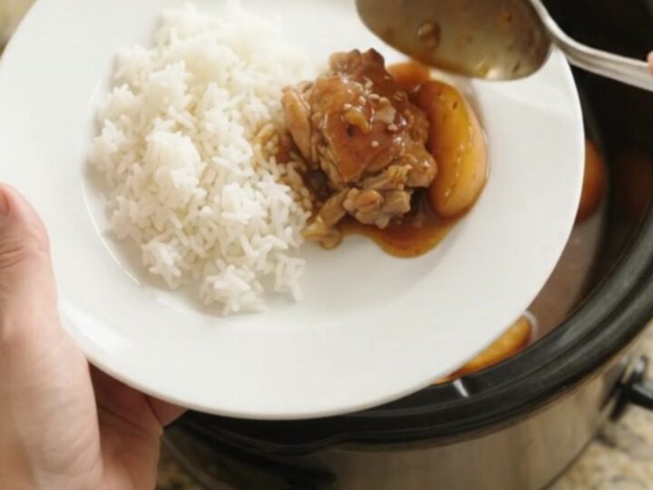 Slow cooker with caramelized peach teriyaki chicken thighs, glistening sauce, sesame seeds