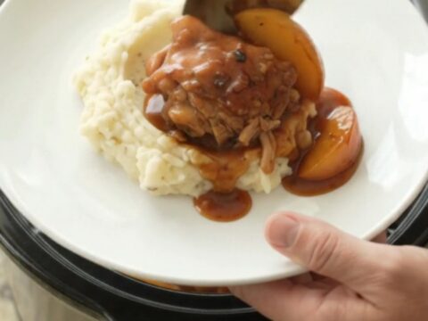 Slow cooker full of glazed chicken thighs and peach slices in a rich bourbon BBQ sauce