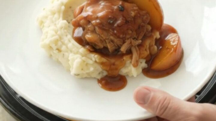 Slow cooker full of glazed chicken thighs and peach slices in a rich bourbon BBQ sauce