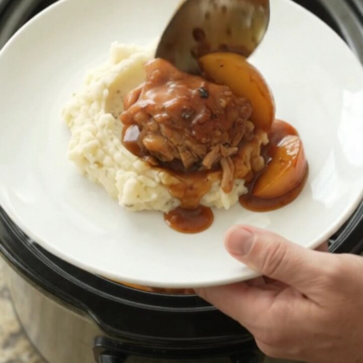 Slow cooker full of glazed chicken thighs and peach slices in a rich bourbon BBQ sauce