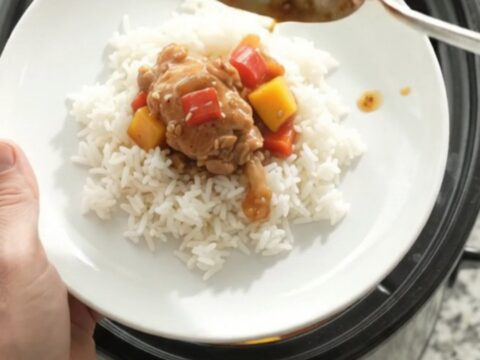 Slow cooker teriyaki mango chicken thighs in a black crockpot with glaze and sesame seeds