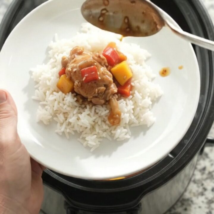 Slow cooker teriyaki mango chicken thighs in a black crockpot with glaze and sesame seeds