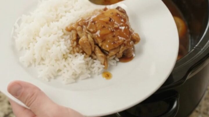 Slow cooker filled with glazed teriyaki chicken thighs and mandarin oranges, topped with sesame seeds