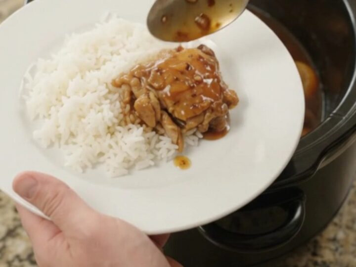 Slow cooker filled with glazed teriyaki chicken thighs and mandarin oranges, topped with sesame seeds