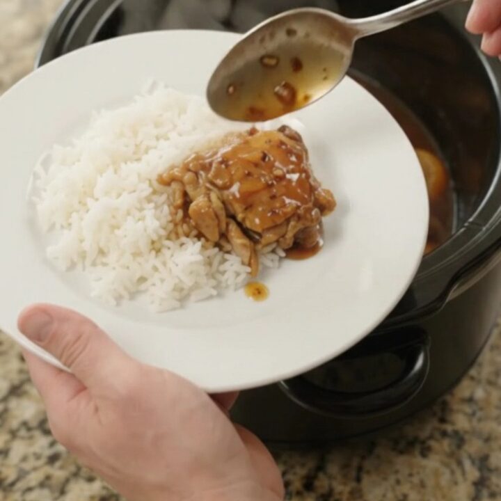 Slow cooker filled with glazed teriyaki chicken thighs and mandarin oranges, topped with sesame seeds