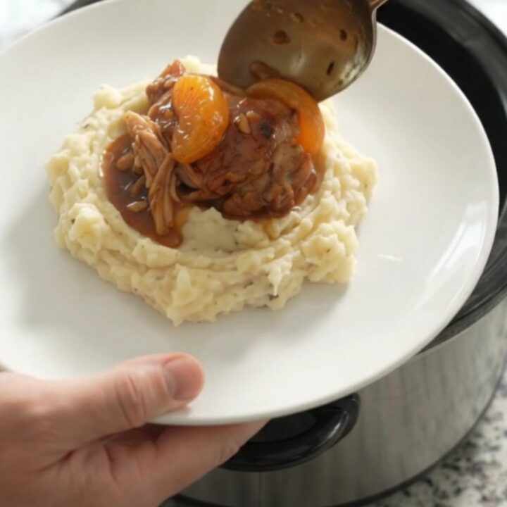 Slow cooker full of glazed chicken thighs with mandarin oranges and bourbon sauce, ready to serve