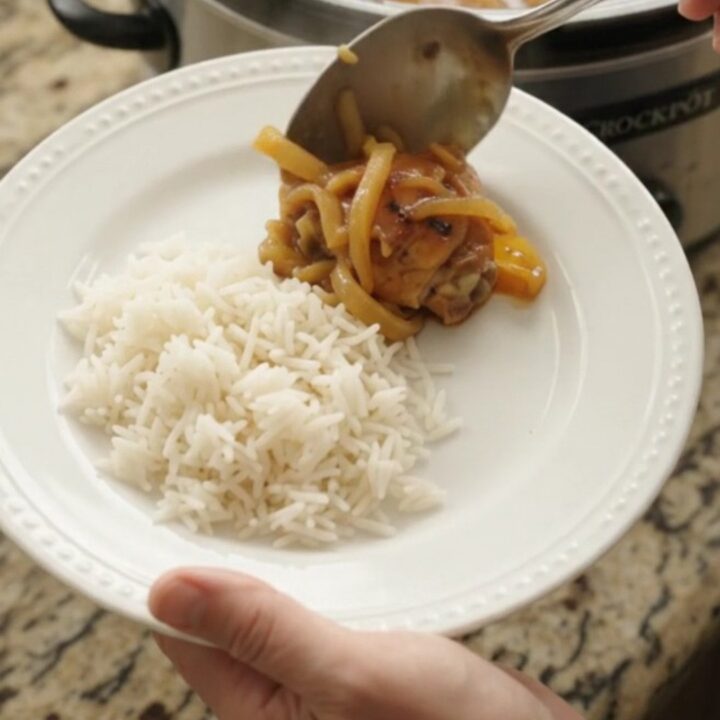 Caramelized pull-apart chicken thighs in a sticky apricot honey soy glaze, served in a black slow cooker.
