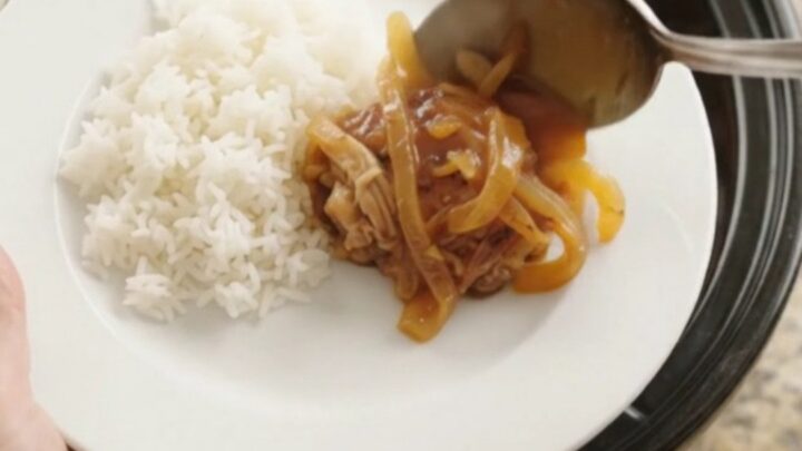 Shredded chicken thighs in a glossy apricot hickory BBQ sauce in a slow cooker, with steam rising