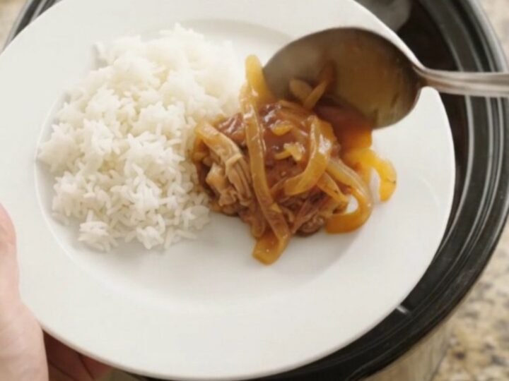 Shredded chicken thighs in a glossy apricot hickory BBQ sauce in a slow cooker, with steam rising
