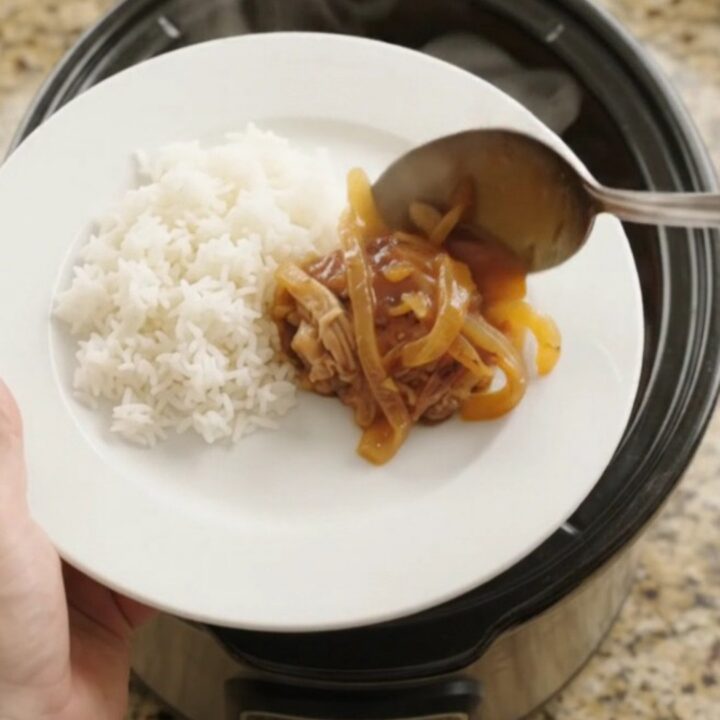 Shredded chicken thighs in a glossy apricot hickory BBQ sauce in a slow cooker, with steam rising