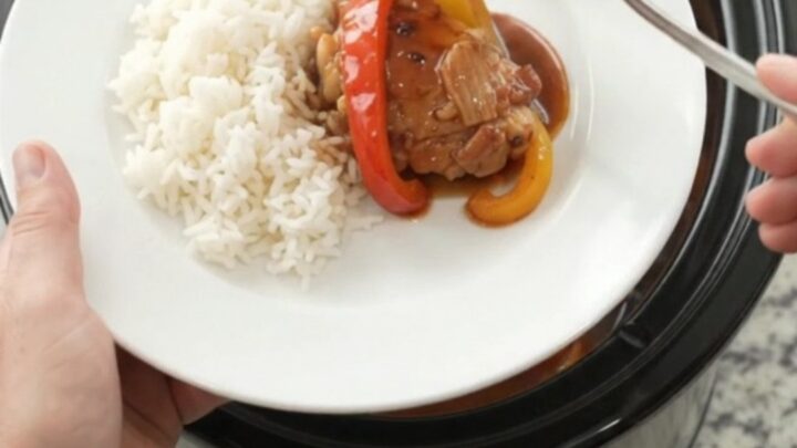 Slow cooker filled with hickory BBQ chicken thighs and bell peppers, glossy sauce, steam rising