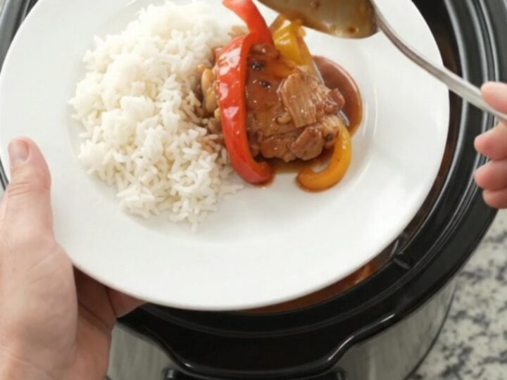 Slow cooker filled with hickory BBQ chicken thighs and bell peppers, glossy sauce, steam rising