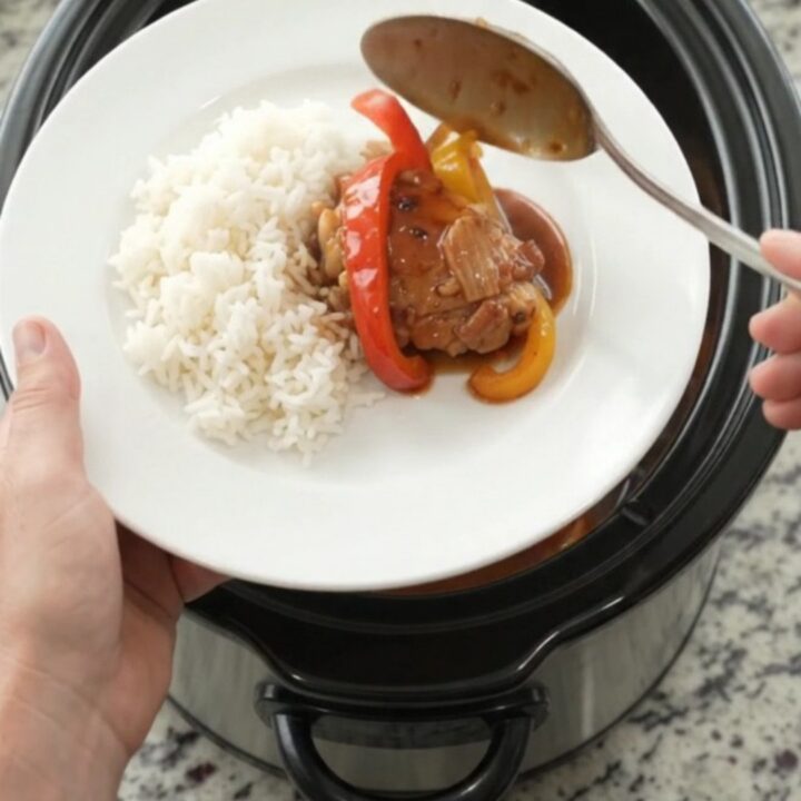 Slow cooker filled with hickory BBQ chicken thighs and bell peppers, glossy sauce, steam rising