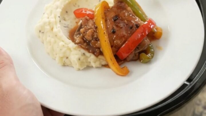 Slow cooker bourbon glazed chicken thighs with bell peppers and onion in a black crockpot
