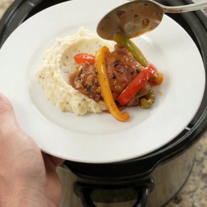 Slow cooker bourbon glazed chicken thighs with bell peppers and onion in a black crockpot