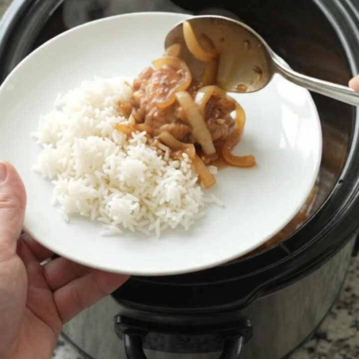 Caramelized chicken thighs with sweet Vidalia onions in a glossy teriyaki glaze, served in a black slow cooker.