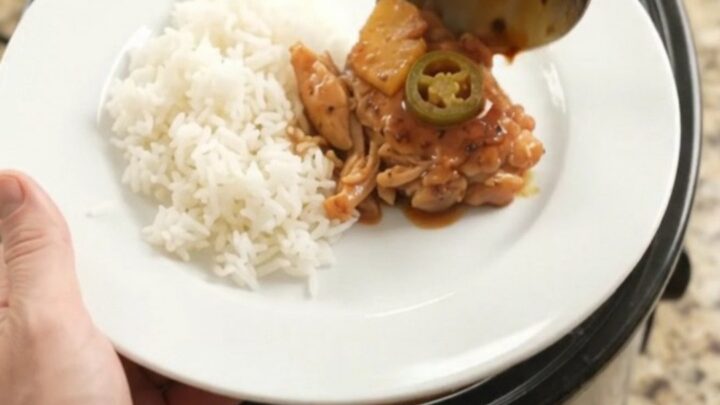 Slow cooker filled with glazed chicken thighs, pineapple tidbits, and jalapeño rings in hickory BBQ sauce