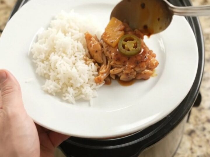 Slow cooker filled with glazed chicken thighs, pineapple tidbits, and jalapeño rings in hickory BBQ sauce