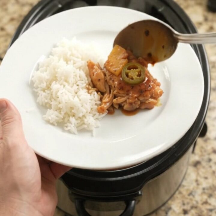 Slow cooker filled with glazed chicken thighs, pineapple tidbits, and jalapeño rings in hickory BBQ sauce