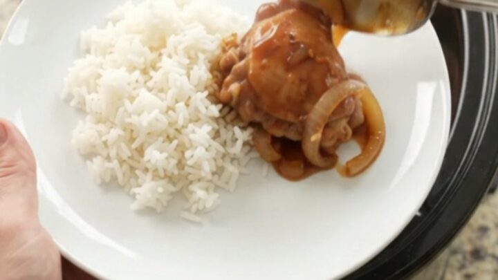 Shredded BBQ chicken thighs in a slow cooker with caramelized onions and glossy sauce