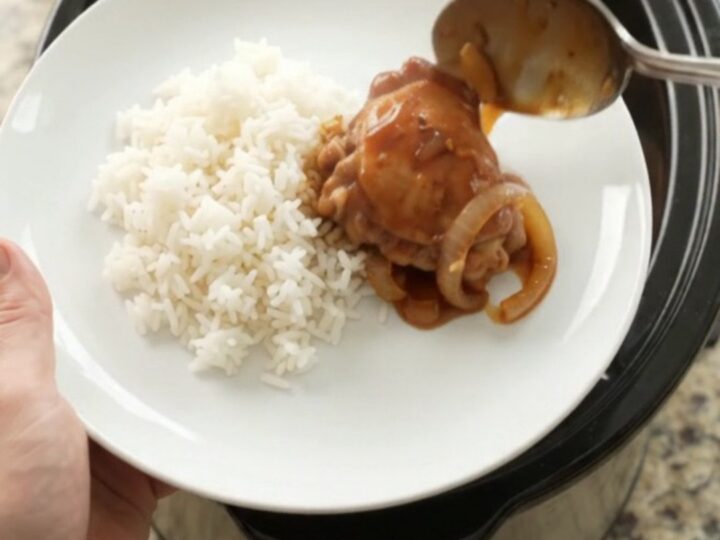 Shredded BBQ chicken thighs in a slow cooker with caramelized onions and glossy sauce