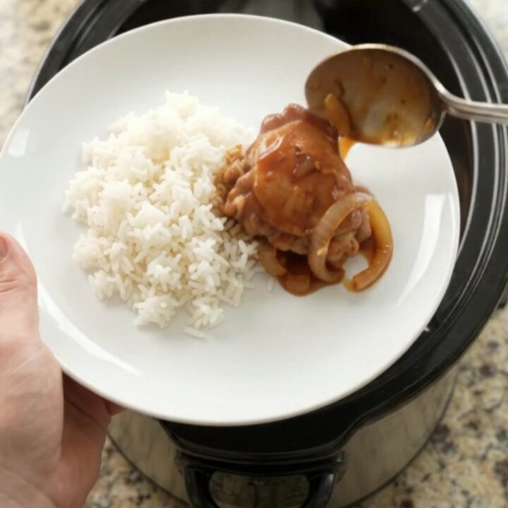 Shredded BBQ chicken thighs in a slow cooker with caramelized onions and glossy sauce