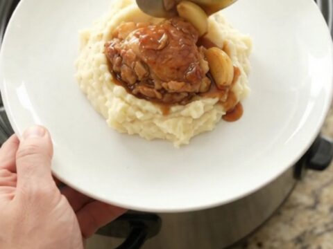 Pull-apart bourbon glazed chicken thighs with garlic cloves in a slow cooker, glossy and caramelized