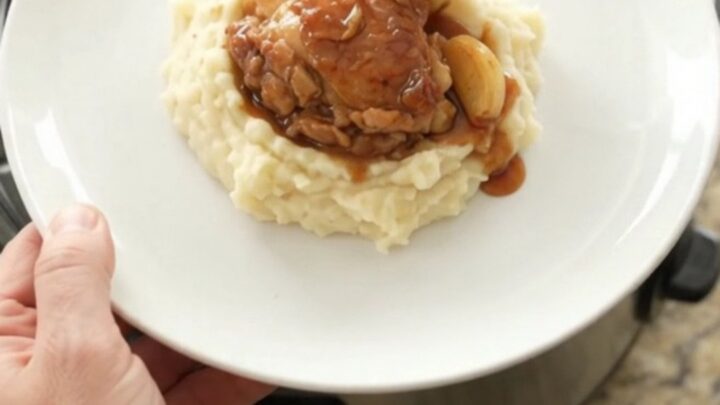 Pull-apart bourbon glazed chicken thighs with garlic cloves in a slow cooker, glossy and caramelized