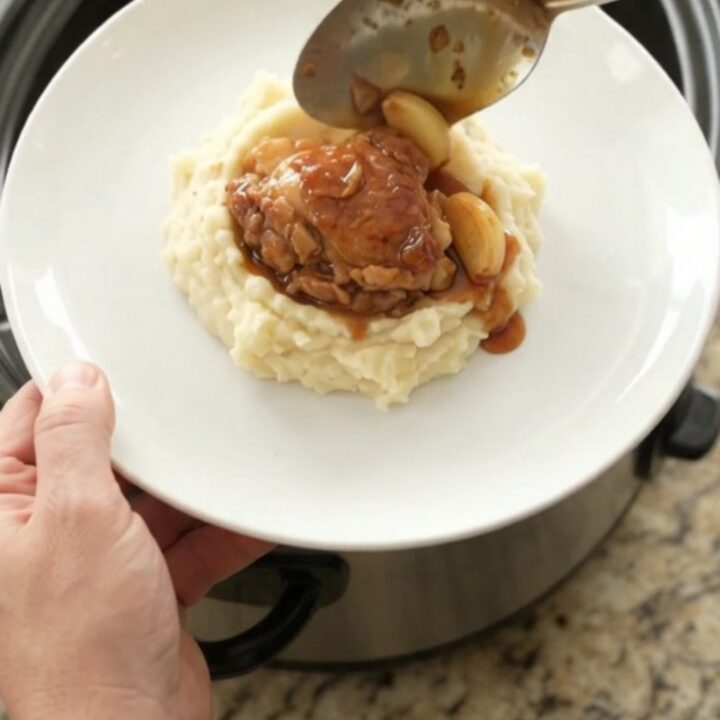 Pull-apart bourbon glazed chicken thighs with garlic cloves in a slow cooker, glossy and caramelized