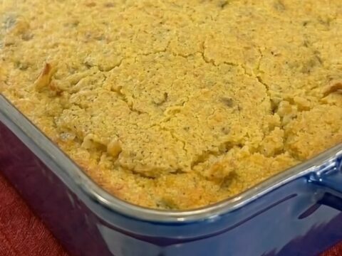A warm scoop of cornbread chicken casserole with a cracked golden crust showing creamy chicken noodles and melted cheese.