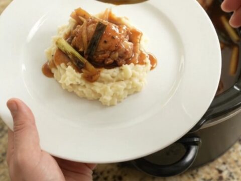 Pull-apart bourbon glazed chicken thighs in a slow cooker, glossy sauce with ginger and scallions