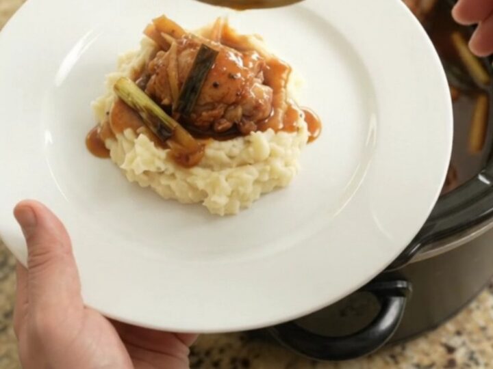 Pull-apart bourbon glazed chicken thighs in a slow cooker, glossy sauce with ginger and scallions