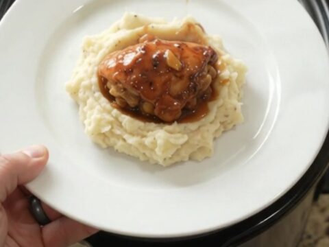 Slow cooker peach bourbon glazed chicken drumsticks in a black crockpot with bubbling sauce and peaches