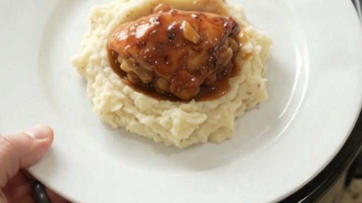 Slow cooker peach bourbon glazed chicken drumsticks in a black crockpot with bubbling sauce and peaches