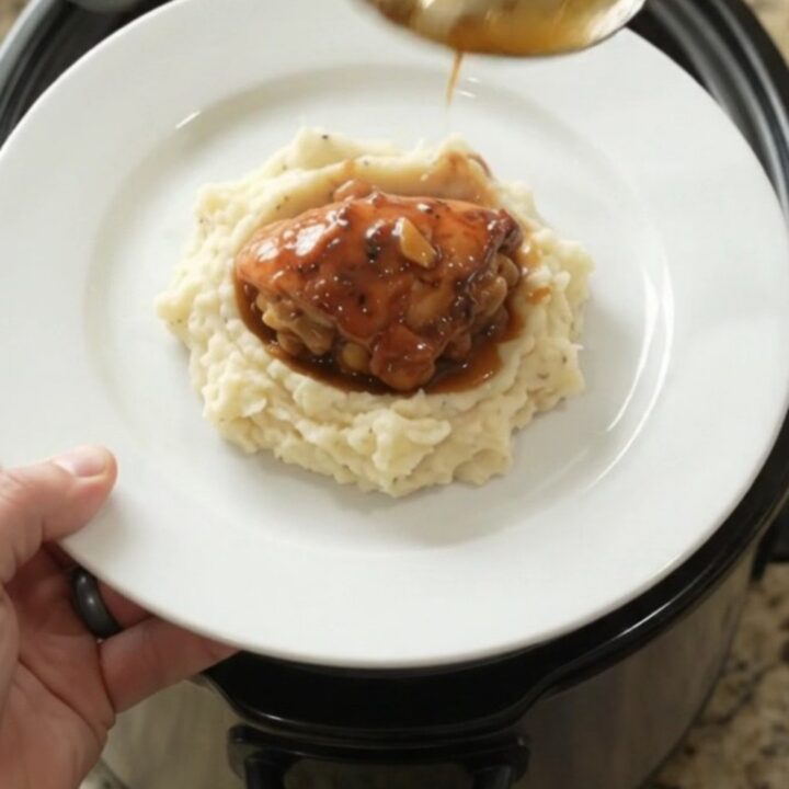 Slow cooker peach bourbon glazed chicken drumsticks in a black crockpot with bubbling sauce and peaches