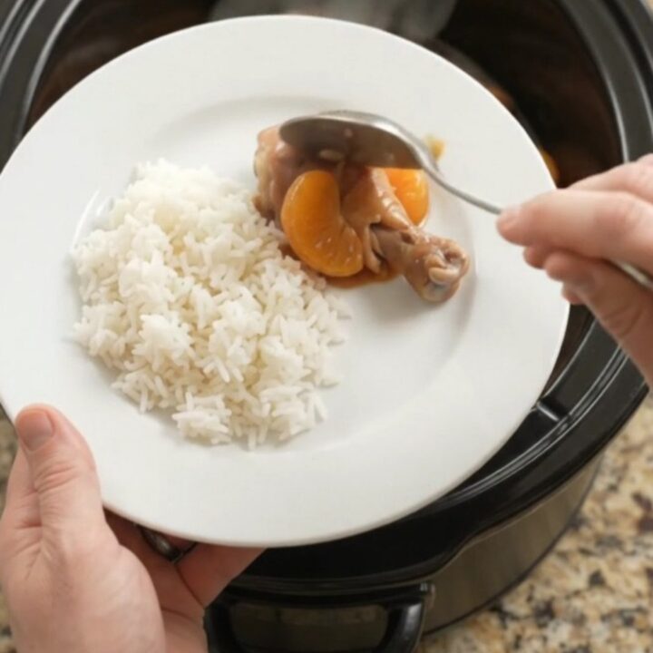 Slow cooker full of glazed chicken drumsticks with mandarin oranges and sesame seeds.