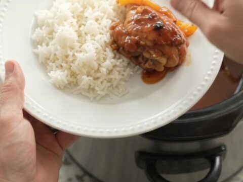 Slow cooker hickory BBQ chicken drumsticks with bell peppers and onions in a dark crockpot.