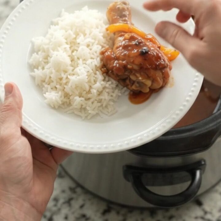 Slow cooker hickory BBQ chicken drumsticks with bell peppers and onions in a dark crockpot.