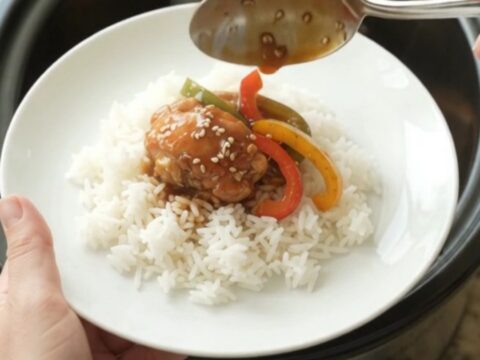 Glossy teriyaki chicken drumsticks on a white platter, garnished with sesame seeds and green onions.