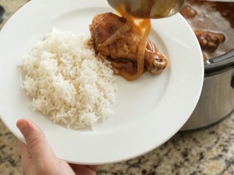 Slow-cooker hickory BBQ chicken drumsticks in a glossy black crockpot, coated in thick sauce with caramelized onions.