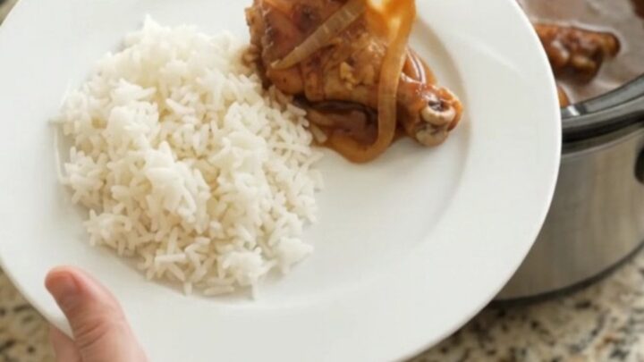 Slow-cooker hickory BBQ chicken drumsticks in a glossy black crockpot, coated in thick sauce with caramelized onions.