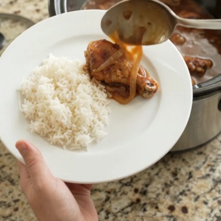 Slow-cooker hickory BBQ chicken drumsticks in a glossy black crockpot, coated in thick sauce with caramelized onions.