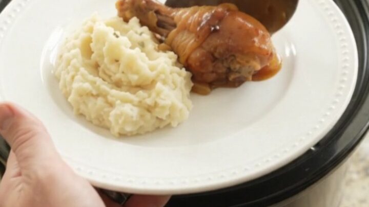 Slow cooker bourbon glazed chicken drumsticks with caramelized Vidalia onions in a black crockpot