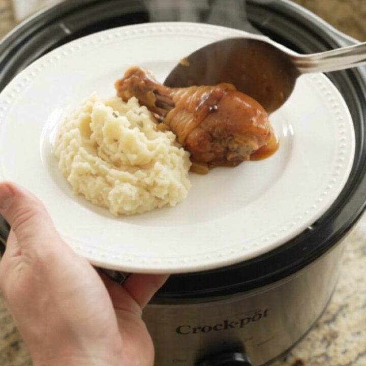 Slow cooker bourbon glazed chicken drumsticks with caramelized Vidalia onions in a black crockpot