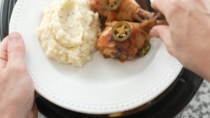 A slow cooker filled with glazed chicken drumsticks, pineapple, and jalapeños