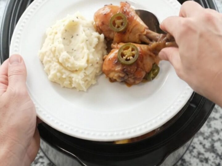 A slow cooker filled with glazed chicken drumsticks, pineapple, and jalapeños