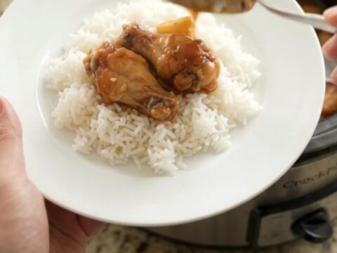 Slow-cooker pineapple teriyaki chicken wings in a black Crockpot, glossy with sauce and sprinkled with sesame seeds.